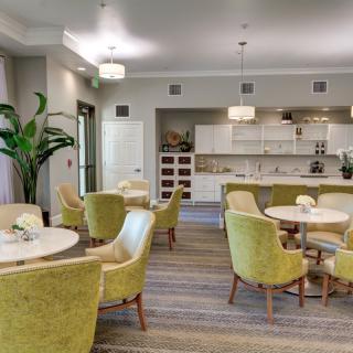 A modern dining area with elegant green chairs and round tables, featuring a stylish kitchen in the background.