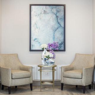 A cozy seating area with two chairs, a small table adorned with flowers, and a framed painting on the wall.