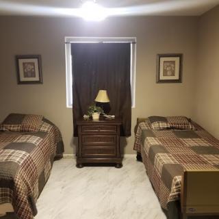 A cozy and simple bedroom featuring twin beds with patterned bedding, a bedside table, and warm lighting.