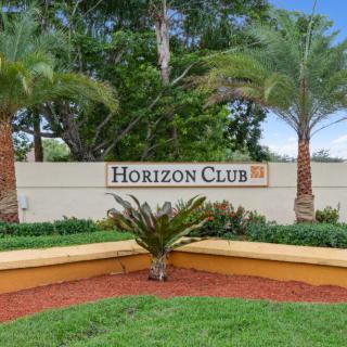 Entrance sign to Horizon Club surrounded by greenery and palm trees.