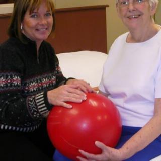 Two women engaged in a physical therapy session with an exercise ball.