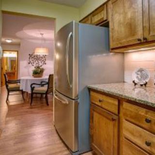 A cozy kitchen with wooden cabinets and a stainless steel refrigerator, opening into a dining area with elegant decor.