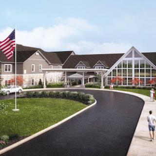 A welcoming entrance to a modern facility surrounded by landscaped gardens and featuring an American flag.