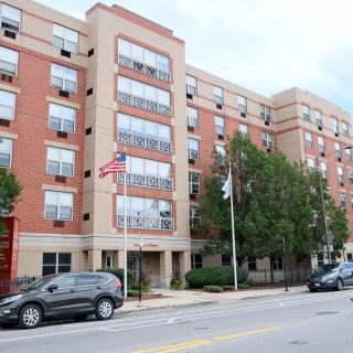A multi-story residential building with trees and parked cars along the street.