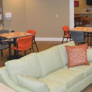 A cozy living space with a green couch, tables, and colorful chairs.