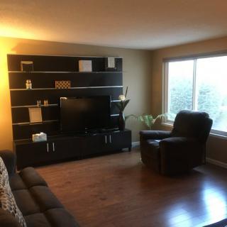 A cozy living room with a TV stand, recliner, and sofa, featuring hardwood floors and ambient lighting.