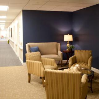A cozy seating area in a hallway with comfortable chairs, a sofa, and a lamp.