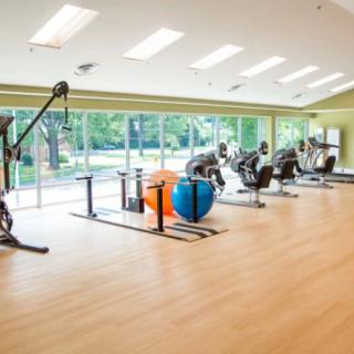 A spacious gym with various exercise equipment and large windows providing natural light.