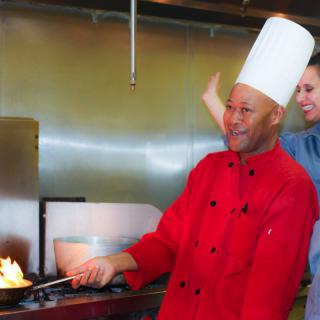 A chef in a red uniform skillfully cooks with a flame in a professional kitchen.