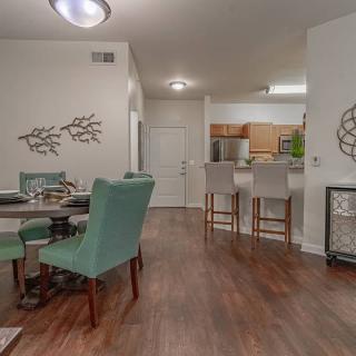 A modern open-concept living space featuring a dining area with turquoise chairs and a kitchen with bar seating.
