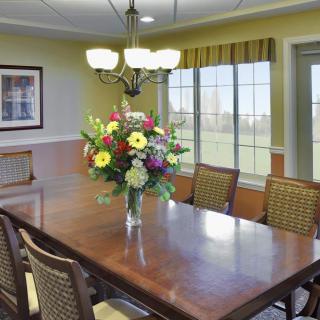 A well-lit dining room with a wooden table, surrounded by chairs, and adorned with a colorful floral centerpiece.