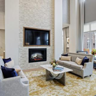 A spacious modern living room featuring a stone fireplace, wall-mounted television, and elegant sofas with decorative pillows.