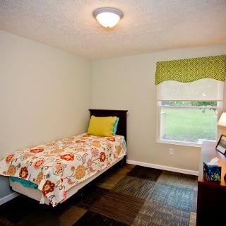 A cozy bedroom with a single bed, colorful bedspread, and a small window letting in natural light.