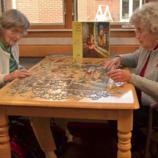 Two elderly women working on a jigsaw puzzle at a table.
