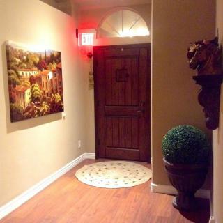 A warmly lit hallway with a decorative entrance door, artwork on the wall, and a potted plant.