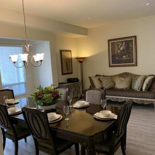 A cozy dining and living area featuring a dining table set for four, a comfortable sofa, elegant artwork, and a chandelier.