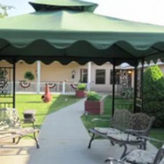 A garden view featuring a gazebo with a green canopy, surrounded by outdoor furniture and a pathway.