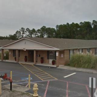A one-story motel building with a parking lot and surrounding trees.