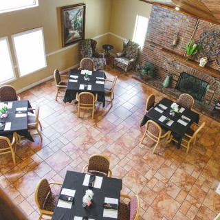 A cozy dining room with neatly arranged tables and chairs, featuring a brick wall and large windows.