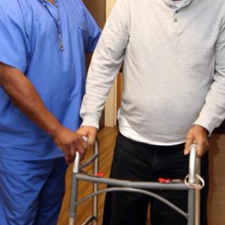 A healthcare worker assists an elderly person using a walker.