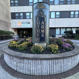 The entrance of Luther Arms, featuring a prominent sign and colorful flower beds.