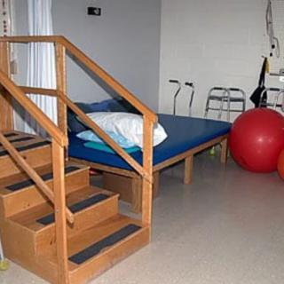 A physical therapy room equipped with stairs, a mat table, crutches, a walker, and an exercise ball.