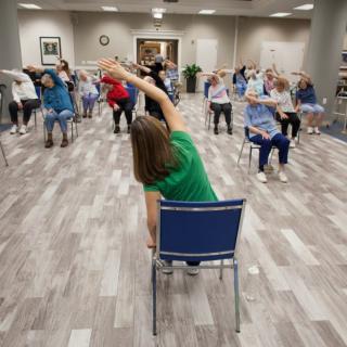 A group of senior citizens participating in a seated exercise class indoors.
