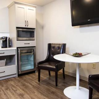 A modern kitchenette with a seating area, featuring sleek appliances and a mounted TV.