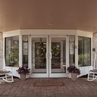 A welcoming entrance with glass doors, flanked by potted plants and rocking chairs.