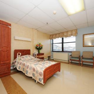A well-lit hospital room featuring a bed, seating area, and decorative flowers.
