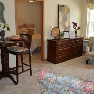 A cozy living room with elegant decor, featuring a wooden dresser, seating area, and artwork.