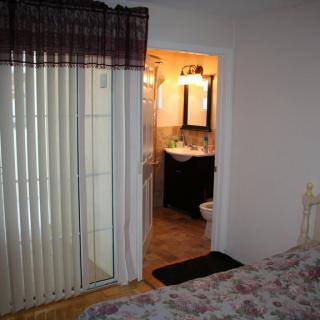 A view from the bedroom into an adjoining bathroom, with vertical blinds on a window or door beside the entrance.