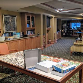 A cozy recreation room with a puzzle on the table and bookshelves in the background.