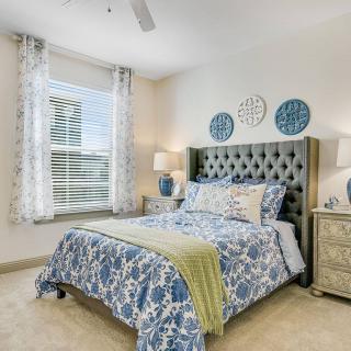 A well-decorated bedroom with blue and white bedding, featuring a tufted headboard, bedside tables with lamps, and decorative wall plates.