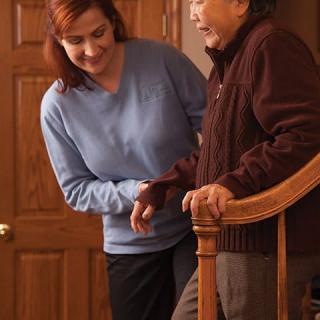 A caregiver assists an elderly person walking up the stairs.