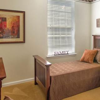 A cozy bedroom with a single bed, a window with blinds, and wall art.