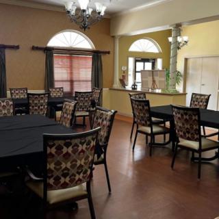 A cozy dining area with round tables and patterned chairs, featuring large windows and warm lighting.