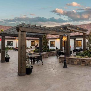 A beautiful outdoor patio with a wooden pergola and seating, set against a sunset sky.