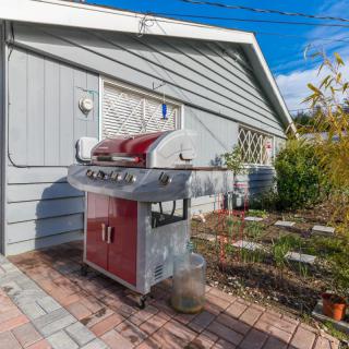 A red and silver barbecue grill on a patio in a backyard garden.