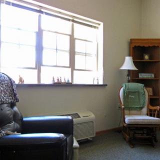 A cozy living room corner with a window, chair, and shelves.