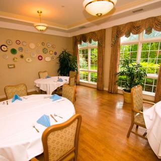 An elegantly set dining room with round tables, natural light streaming through large windows, and tasteful wall decor.
