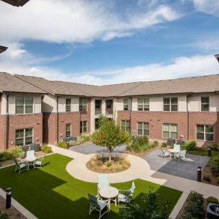 A well-maintained courtyard with seating areas, surrounded by a brick building under a clear blue sky.