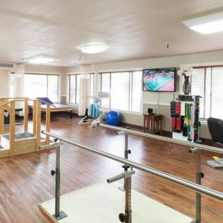 A spacious rehabilitation center with exercise equipment, parallel bars, and a television for patient use.