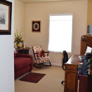 A cozy living room and home office combination with a comfortable sofa, rocking chair, and desk next to a bright window.