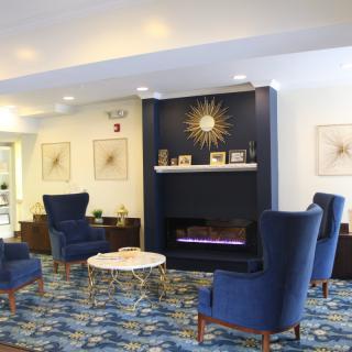 A modern lobby with blue chairs and a decorative fireplace, featuring stylish decor and a patterned carpet.