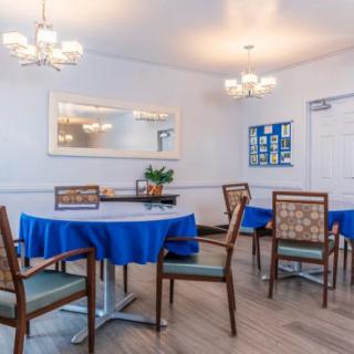 A cozy dining area with tables covered in blue tablecloths and surrounded by wooden chairs, illuminated by elegant chandeliers.