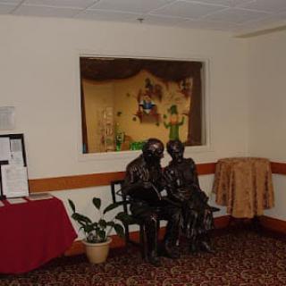 Interior room featuring a sculpture of two figures sitting together, surrounded by artistic decor and plants.