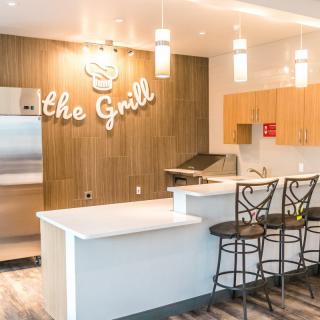 A modern kitchen area with bar stools and a grill setup, featuring stylish wood paneling and pendant lights.
