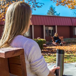 A tranquil autumn day where one person enjoys their beverage while seated on a bench, and another relaxes in the background.