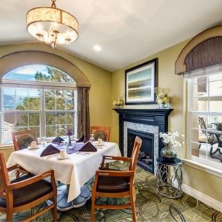 A cozy dining room with a table set for four, featuring a chandelier and a fireplace.